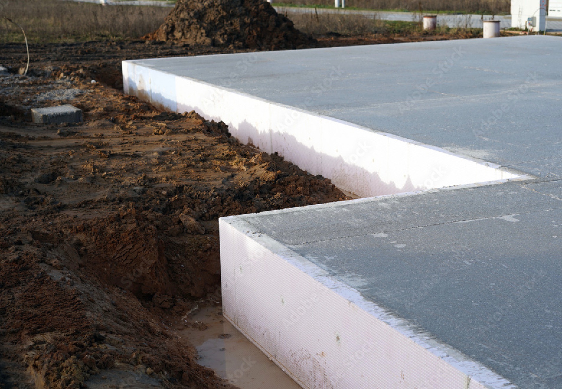 Przygotowany fundament z izolacją termiczną na budowie w Warszawie, widok z poziomu gruntu na wykopany rów wokół fundamentu.