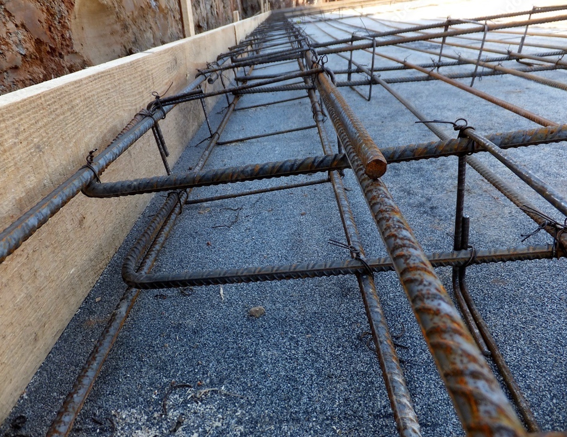Zbrojenie płyty fundamentowej z widocznymi prętami zbrojeniowymi połączonymi drutem wiązałkowym, drewniane szalunki wzdłuż krawędzi.