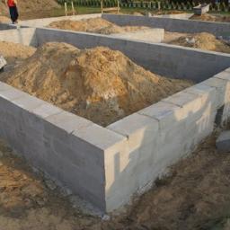 Ew-Dom - Fundamenty domu z bloczków betonowych, zasypane piaskiem, widok z góry na narożnik konstrukcji, etap budowy.