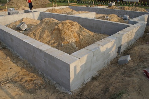 Fundamenty domu z bloczków betonowych, zasypane piaskiem, widok z góry na narożnik konstrukcji, etap budowy.