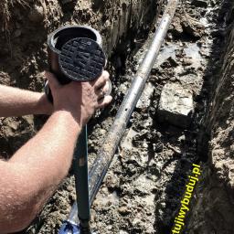 Zaprojektuj i Wybuduj Sp. z o.o. - Montaż studzienki wodomierzowej w wykopie, widoczna rura wodociągowa i narzędzia, teren budowy.