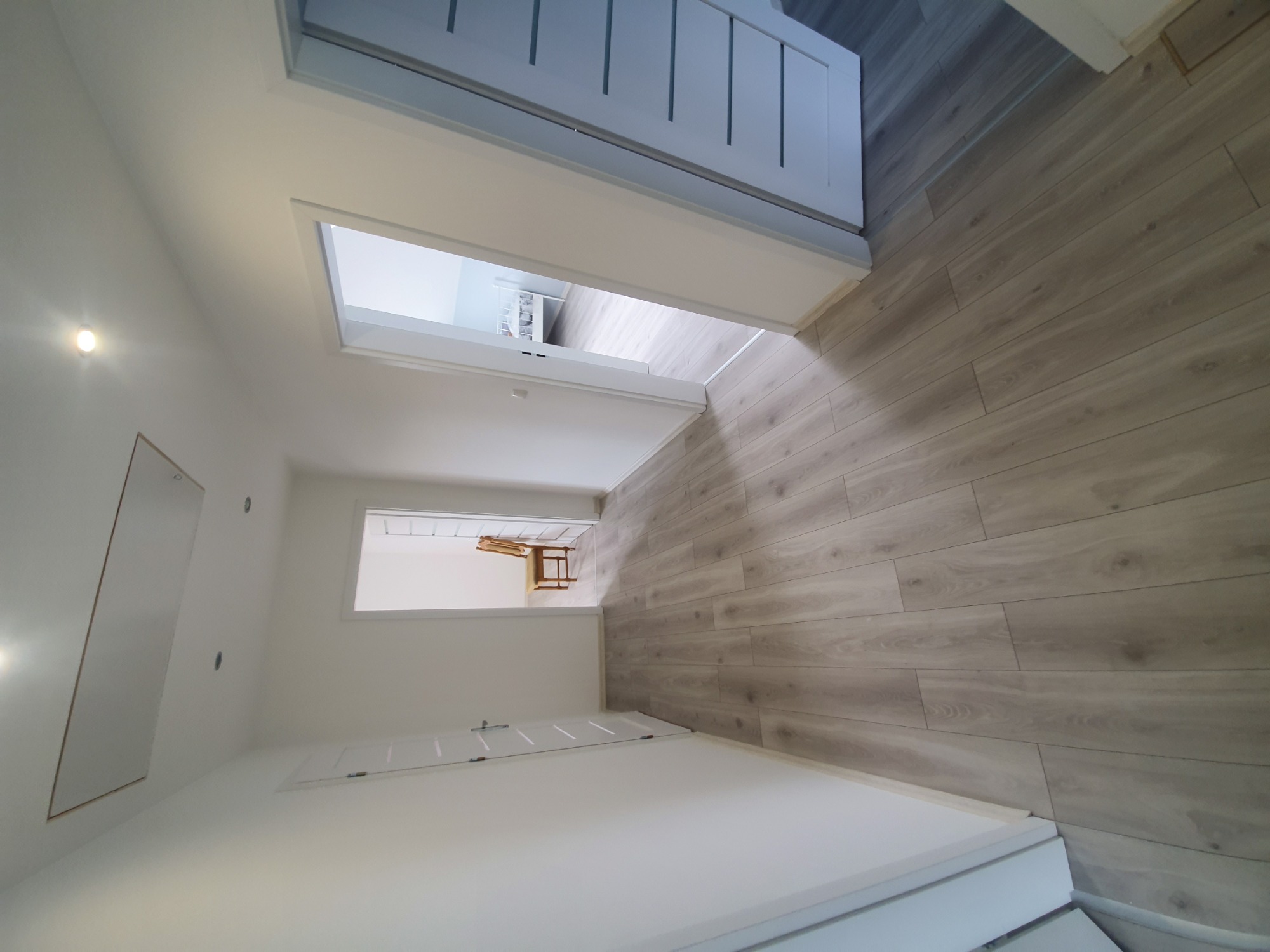 Korytarz w jasnych kolorach z panelami podłogowymi imitującymi drewno, widok z góry na otwarte drzwi do kolejnych pomieszczeń.