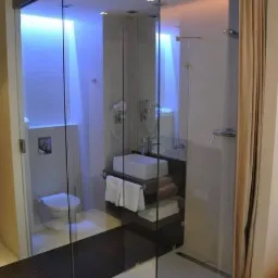 Nowoczesna łazienka z kabiną prysznicową oddzieloną szklaną ścianą, podświetlona na niebiesko, z elementami dekoracyjnymi z białych kamieni na podłodze.