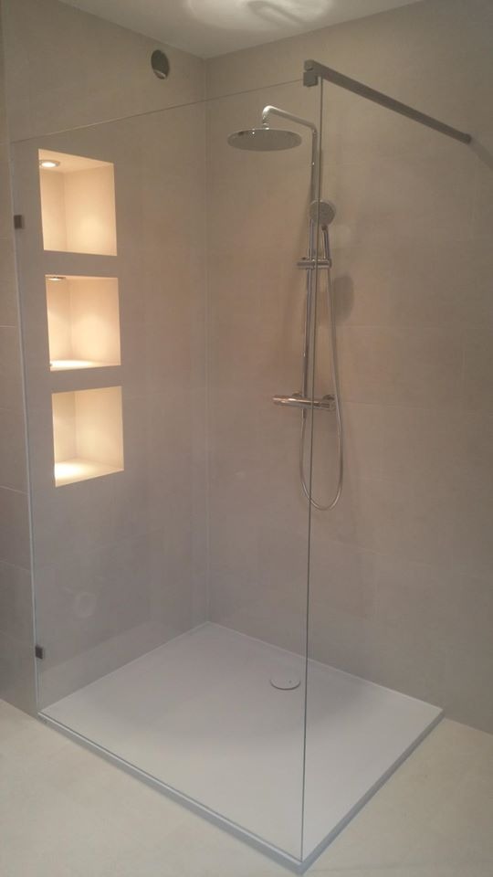 Nowoczesna kabina prysznicowa z płaskim brodzikiem, szklaną ścianą i wnękami oświetlonymi punktowo w ścianie.