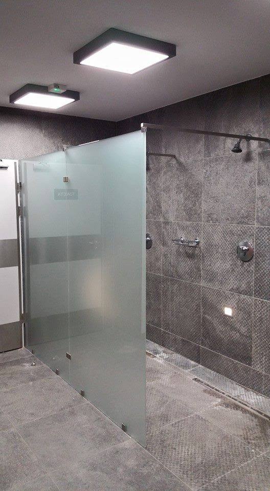 Szklana kabina prysznicowa z matowym szkłem, zamontowana w nowoczesnej łazience z szarymi płytkami, widoczne chromowane baterie i deszczownica.