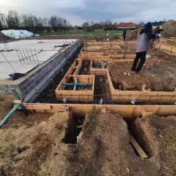 Przygotowanie zbrojenia i szalunków pod fundamenty w Legnicy, widoczne wystające pręty i drewniane formy.