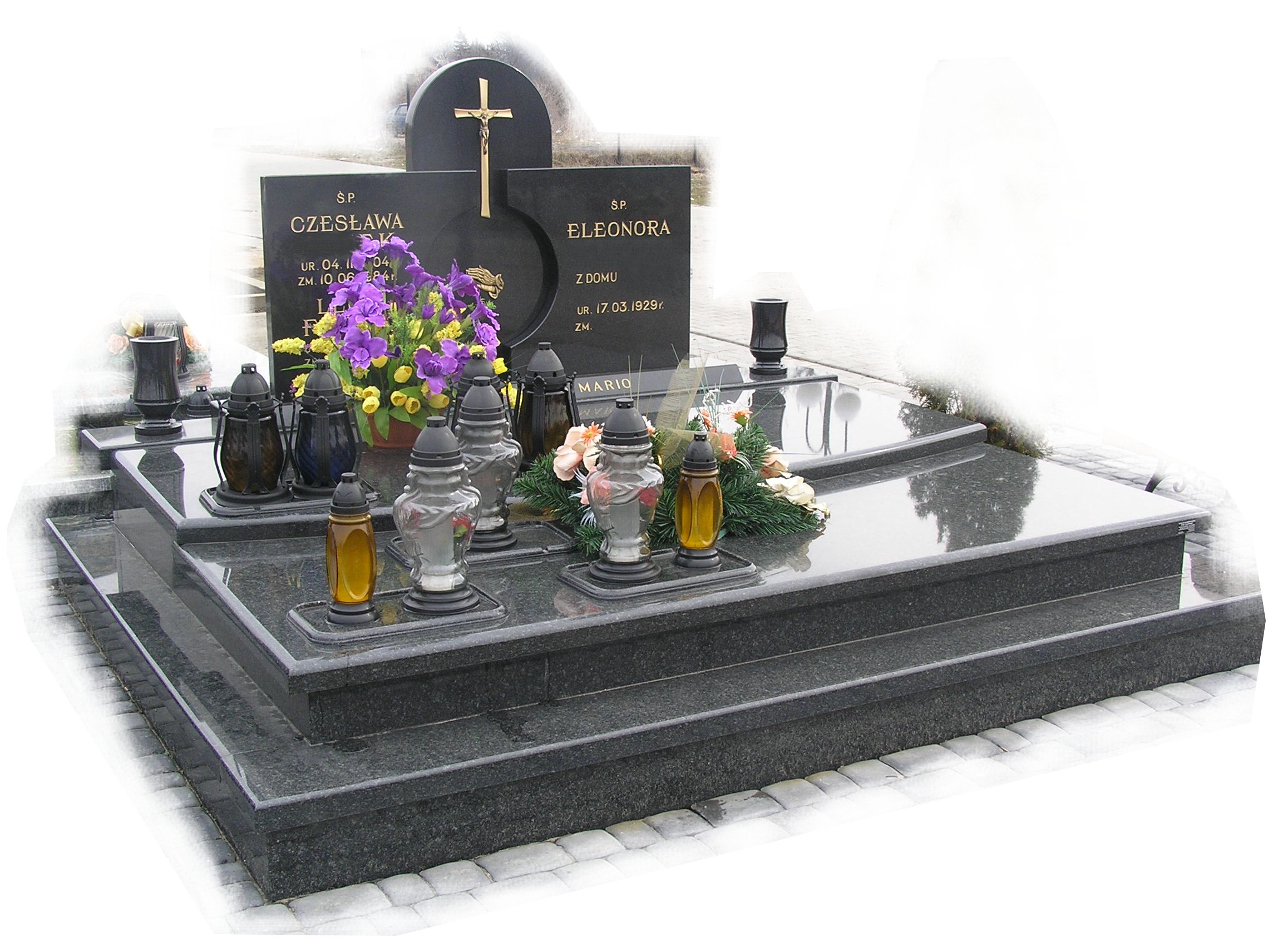 Granitowy pomnik z dwoma tablicami nagrobnymi, lampionami i kwiatami, widok z perspektywy lekko z dołu.