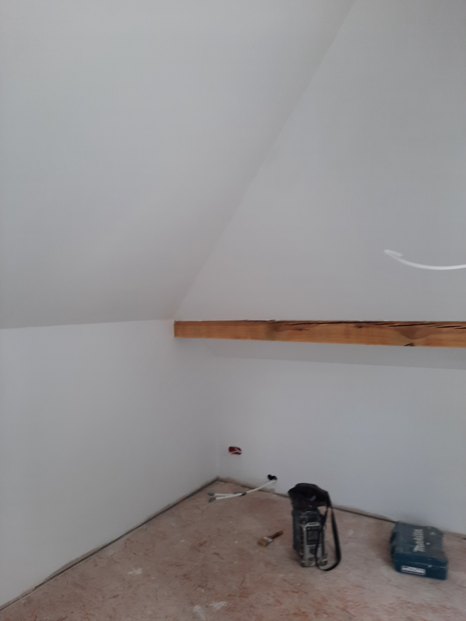 Poddasze w Mrowinie po malowaniu, widoczna drewniana belka stropowa, białe ściany i podłoga przygotowana do dalszych prac wykończeniowych, narzędzia malarskie i skrzynka narzędziowa na podłodze.