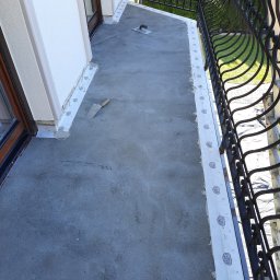 FLIZ-DEM - Balkon w trakcie wylewki posadzki, z widocznymi łatami i szpachelkami, zabezpieczony przy ścianach taśmą izolacyjną Ardex, z ozdobną kutą balustradą w tle.