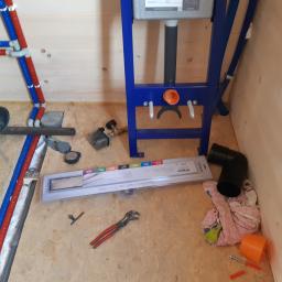 FLIZ-DEM - Montaż stelaża podtynkowego i odpływu liniowego w łazience w Jordanowie, widoczne rury doprowadzające wodę, narzędzia i elementy instalacji przed położeniem płytek.