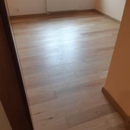 FLIZ-DEM - Jasne panele podłogowe ułożone w pokoju z grzejnikiem pod oknem, widoczne z perspektywy wejścia.