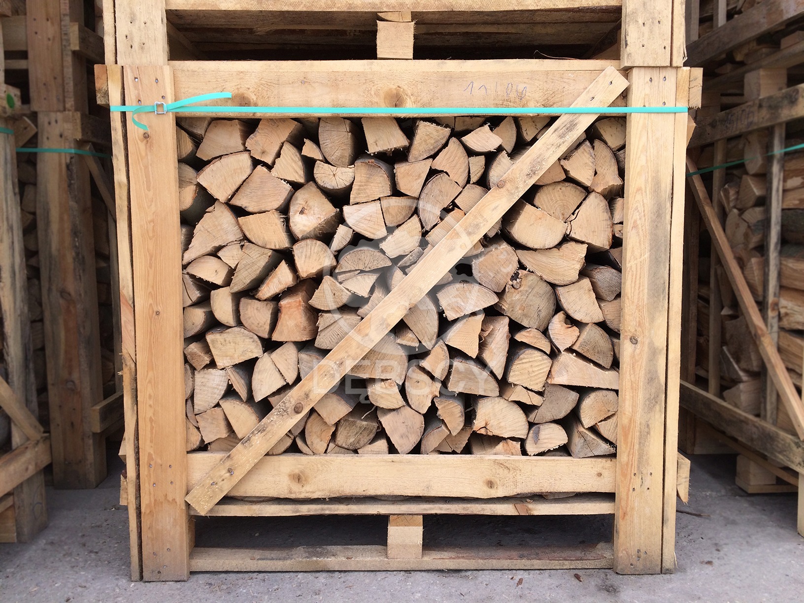 Drewno kominkowe pocięte na kawałki, ułożone w drewnianej skrzyni transportowej, zabezpieczone niebieską taśmą i drewnianą listwą na skos.
