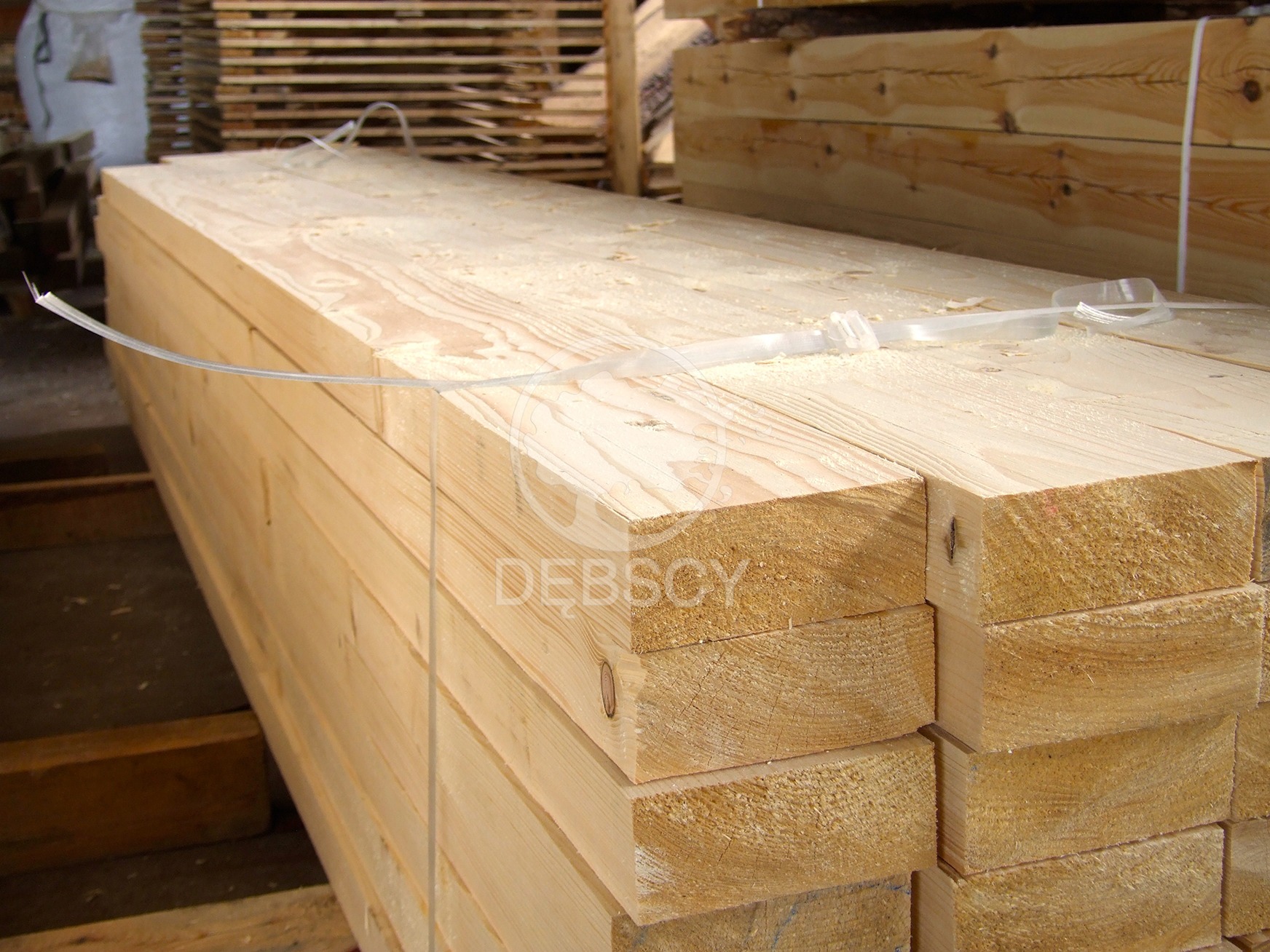 Stos jasnej, świeżo przetartej kantówki z widocznym rysunkiem słojów drewna, spięty plastikową taśmą, leżący na palecie w magazynie.