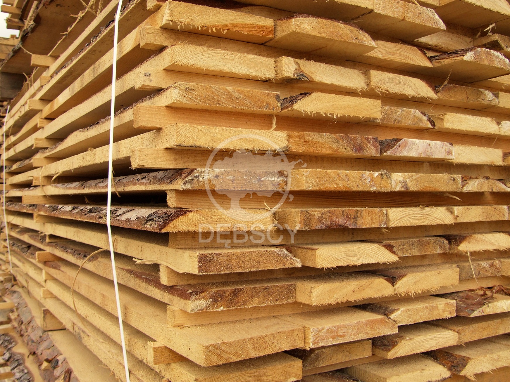 Stos tarcicy budowlanej z widoczną korą na krawędziach, zabezpieczony białą taśmą.