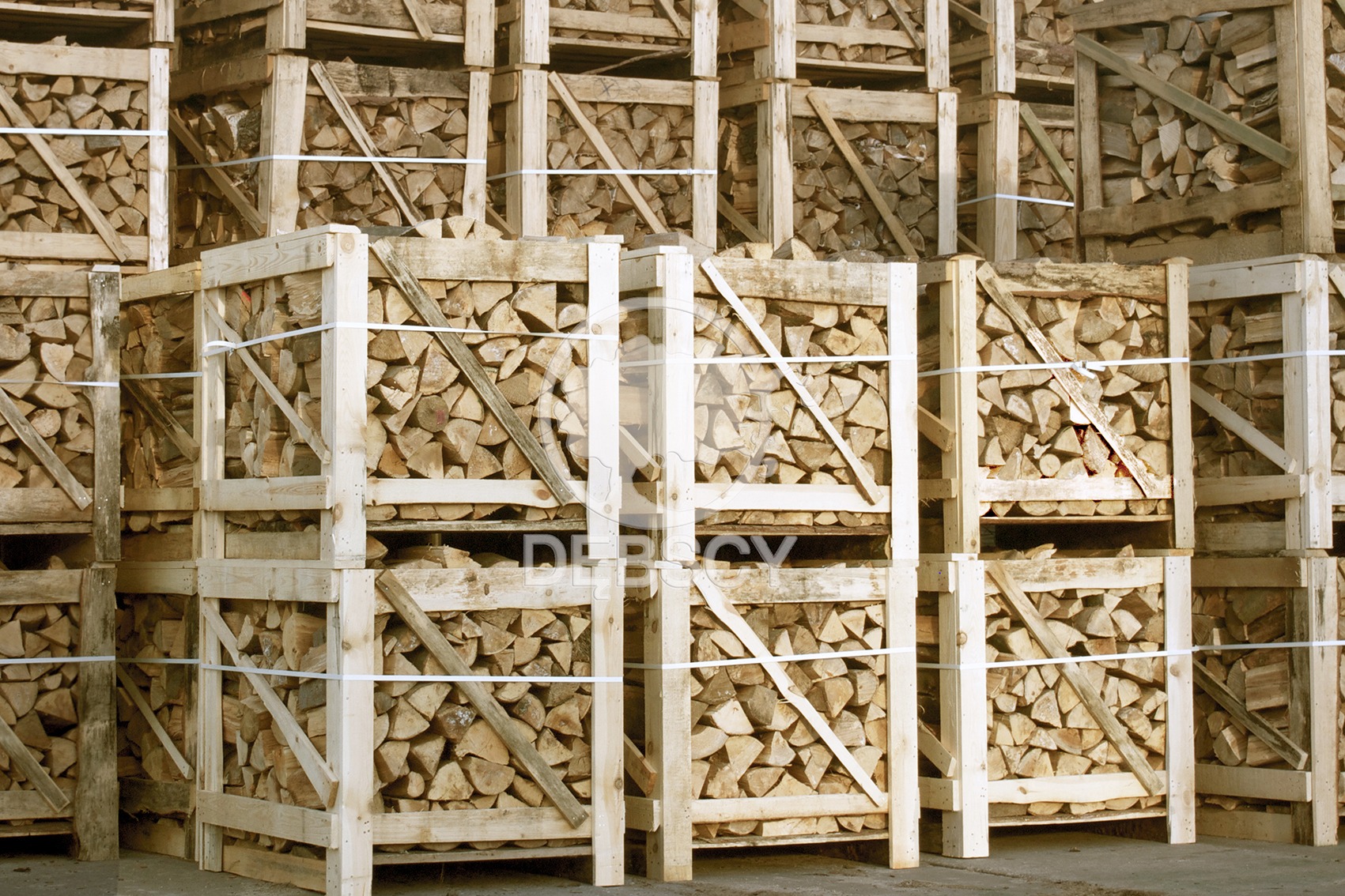 Ułożone w stos drewniane skrzynie wypełnione pociętym drewnem opałowym, zabezpieczone białym sznurkiem, widok z bliska na betonowej posadzce.