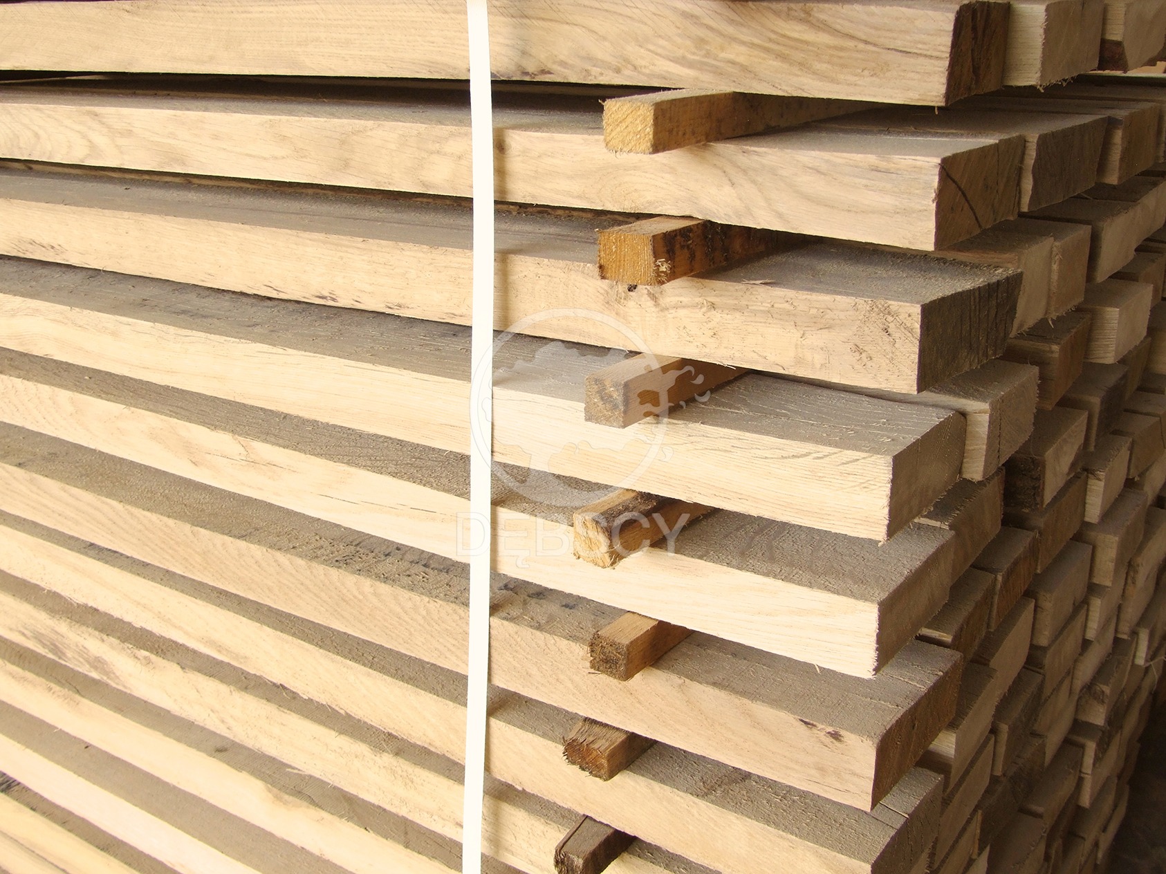 Stos jasnej, świeżo przetartej tarcicy ułożonej warstwami, zabezpieczony białą taśmą, widoczne słoje drewna.