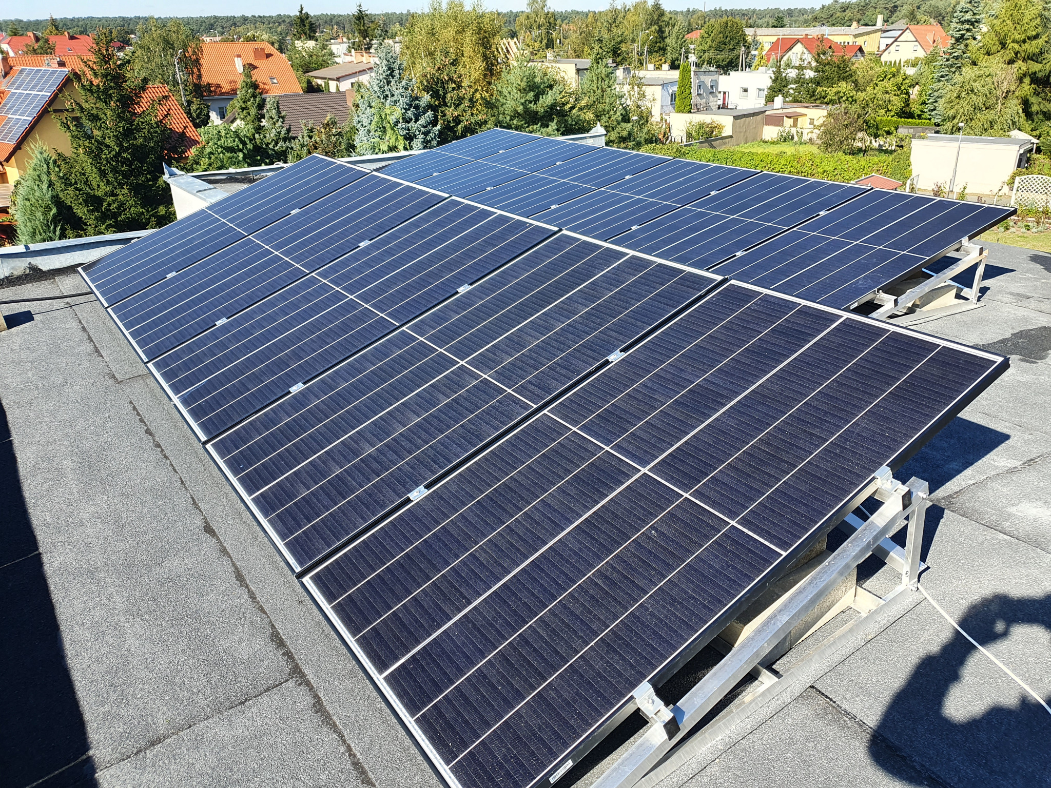 Instalacja paneli słonecznych na dachu budynku w Chodzieży, widok z góry, metalowa konstrukcja wsporcza paneli, w tle zabudowa jednorodzinna i zieleń.