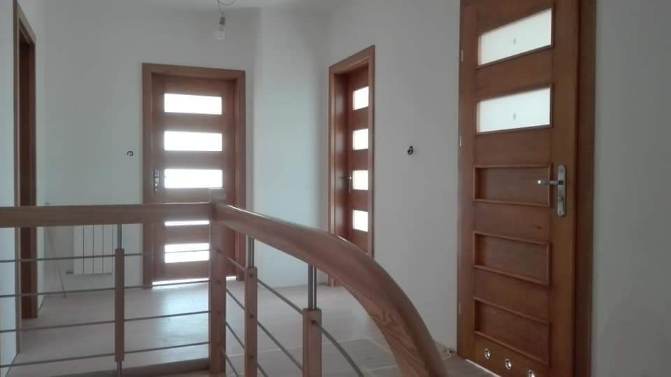 Korytarz z trzema drewnianymi skrzydłami wewnątrz budynku w Śmigiel, z których jedno ma przeszklenia, widok z góry schodów z drewnianą barierką.