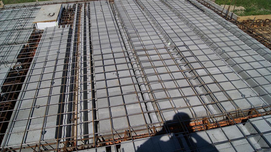 Zbrojenie stropu Teriva z pustakami betonowymi, widoczne elementy szalunku i cień osoby fotografującej.