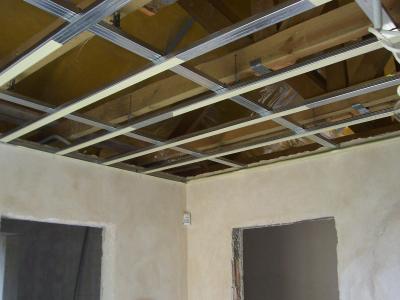 Wnętrze w trakcie remontu: sufit z metalową konstrukcją podwieszaną i surowymi ścianami przed malowaniem, widoczne drewniane elementy stropu.
