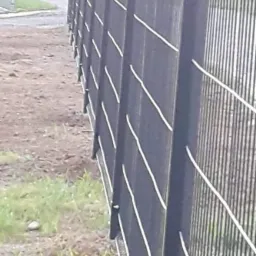 Ciemnoszare ogrodzenie panelowe z białymi akcentami, widoczne słupki i przęsła, trawa u podstawy, perspektywa z boku.