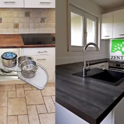 Kuchenne szafki z białymi frontami i szarobrązowym blatem, widoczny narożny system wysuwny z garnkami i talerzami oraz czarny zlew z chromowaną baterią na blacie z ciemnego drewna. W tle logo firmy...