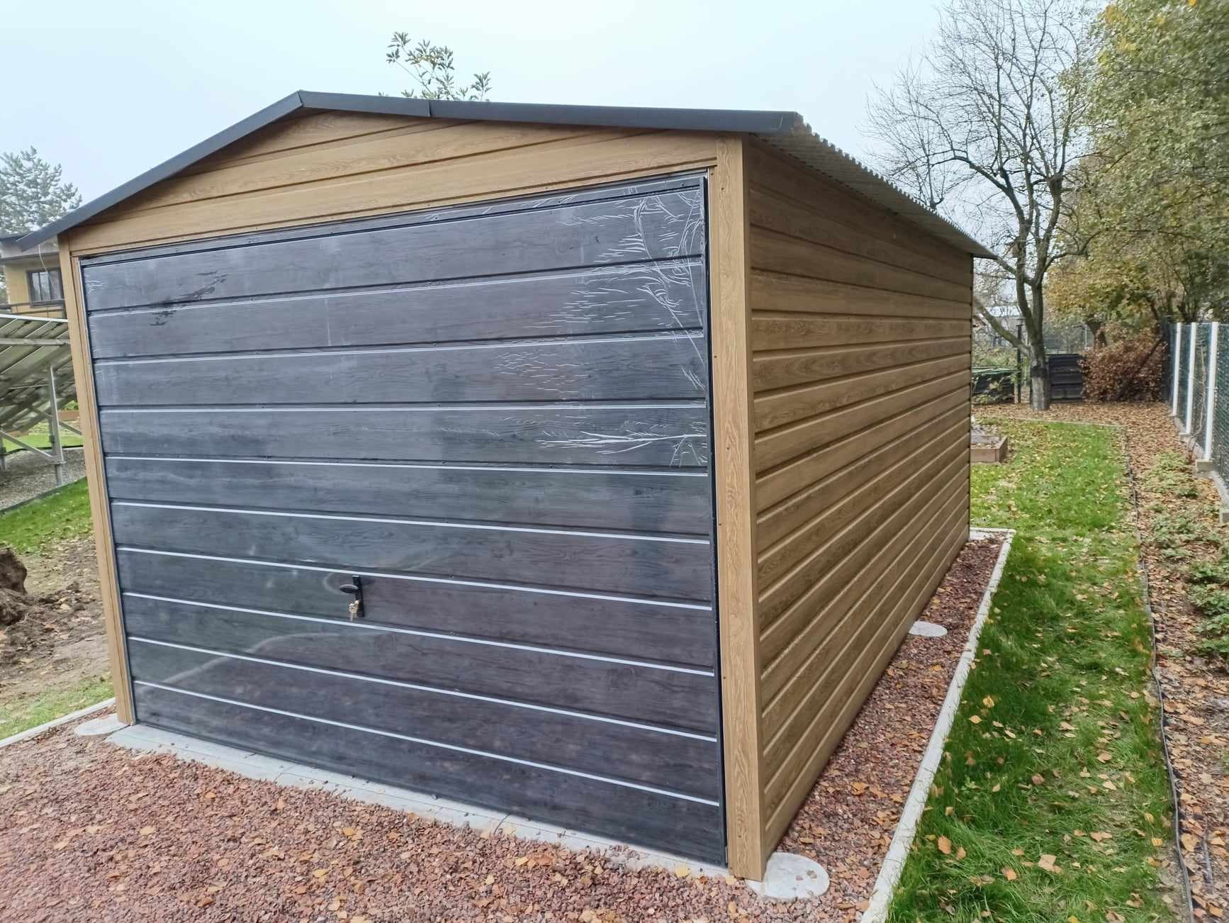 Gotowy garaż blaszany w Tarnawie, z brązowymi ścianami i szarą, poziomą bramą segmentową z folią ochronną. Widoczny zamek w bramie i otoczenie z trawnikiem i brązowym żwirem.