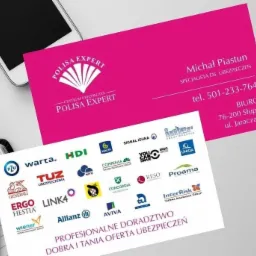 Dwie wizytówki na biurku obok smartfona. Górna wizytówka w kolorze fuksji z danymi kontaktowymi i logo 'Polisa Expert'. Dolna wizytówka biała z logo wielu firm ubezpieczeniowych oraz hasłem...