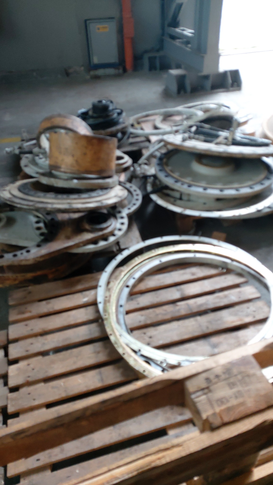 Stos metalowych elementów z otworami na drewnianej palecie w hali przemysłowej, widoczne ślady użytkowania i korozji.