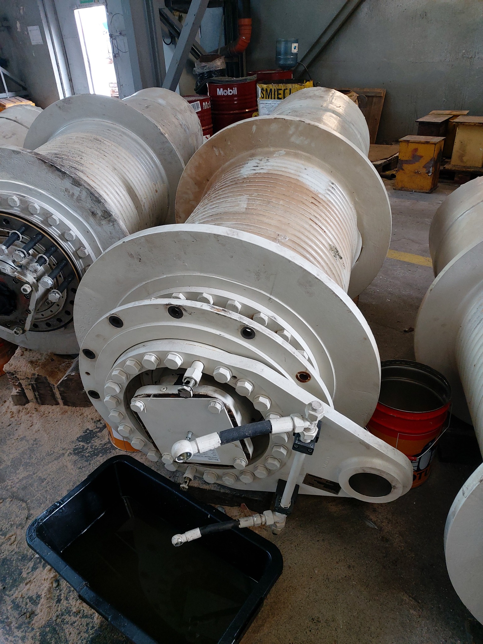 Bębny linowe z hydraulicznym systemem sterowania, widoczna czarna kuweta z olejem, w tle beczki z olejem Mobil