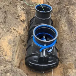 Czarny, plastikowy zbiornik bezodpływowy z niebieskimi elementami instalowany w wykopie ziemnym.