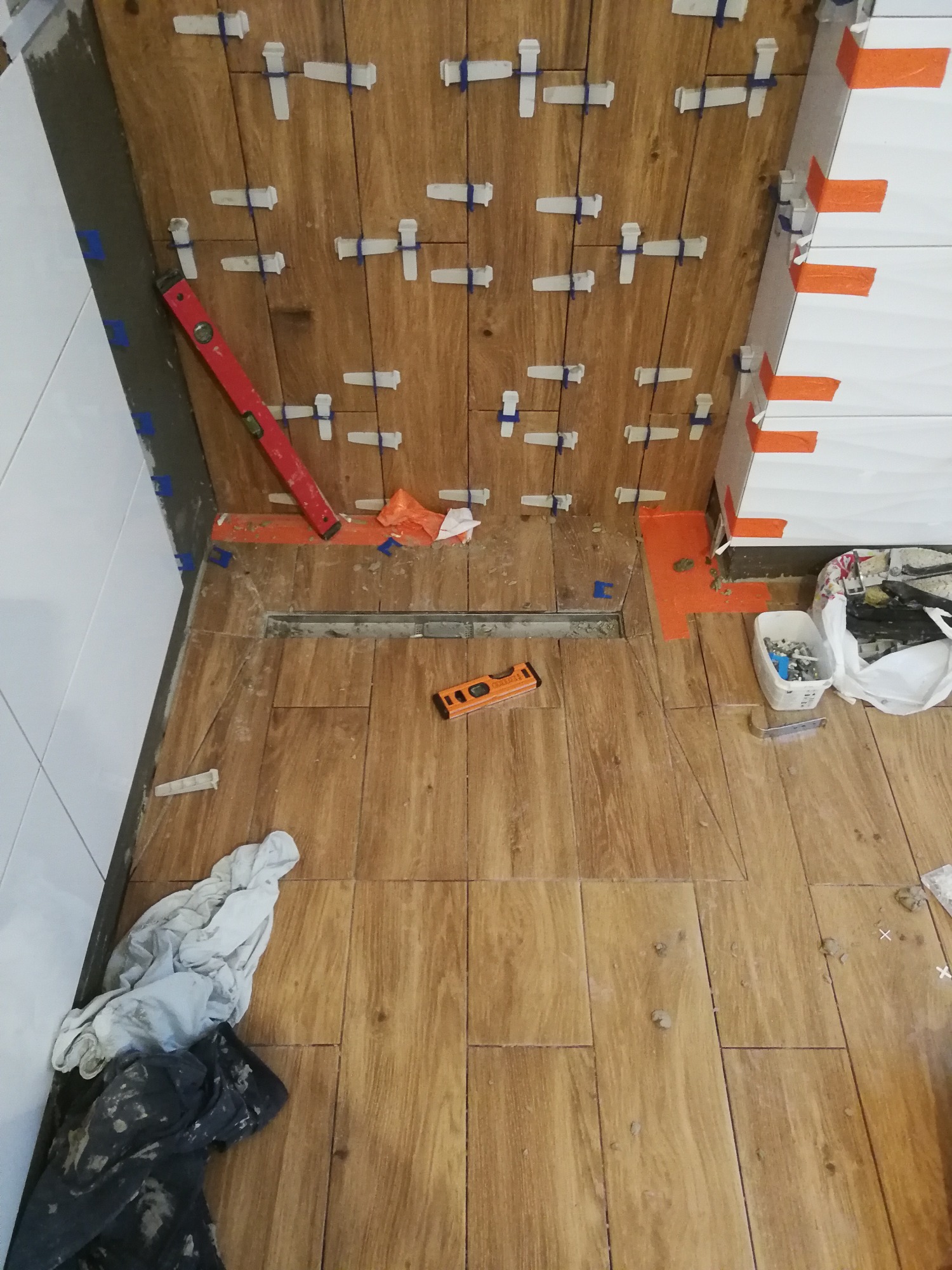 Układanie płytek imitujących drewno w łazience, widoczny odpływ liniowy, poziomica, krzyżyki dystansowe i taśma malarska.