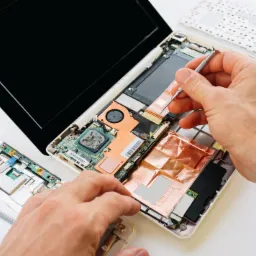 Otwarty laptop z widocznymi podzespołami, demontowany za pomocą precyzyjnego śrubokręta, obok odpięta klawiatura i obudowa.