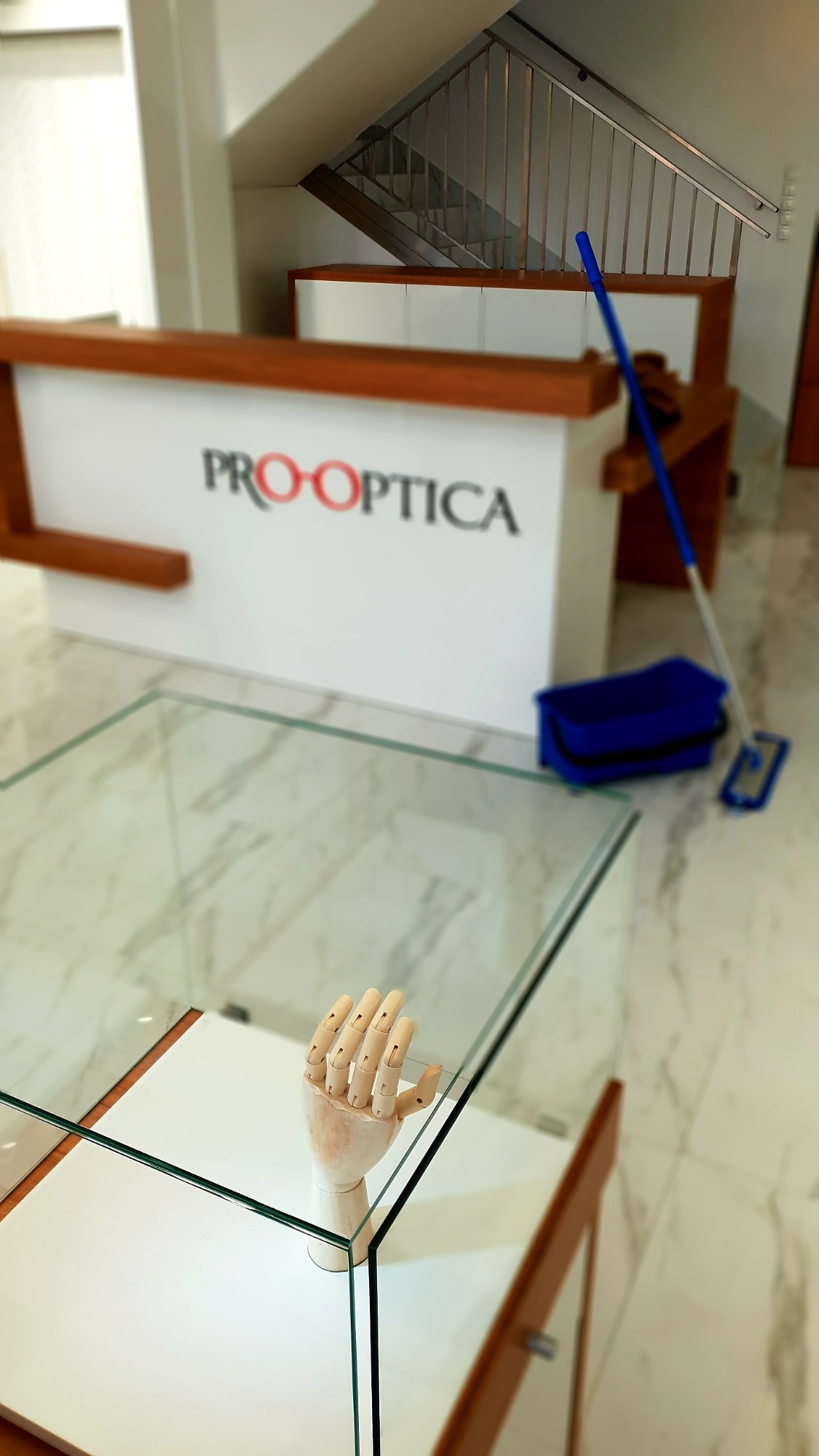 Wnętrze biura z recepcją, mopem i wiadrem, drewniana ręka na szklanej witrynie, marmurowa podłoga.