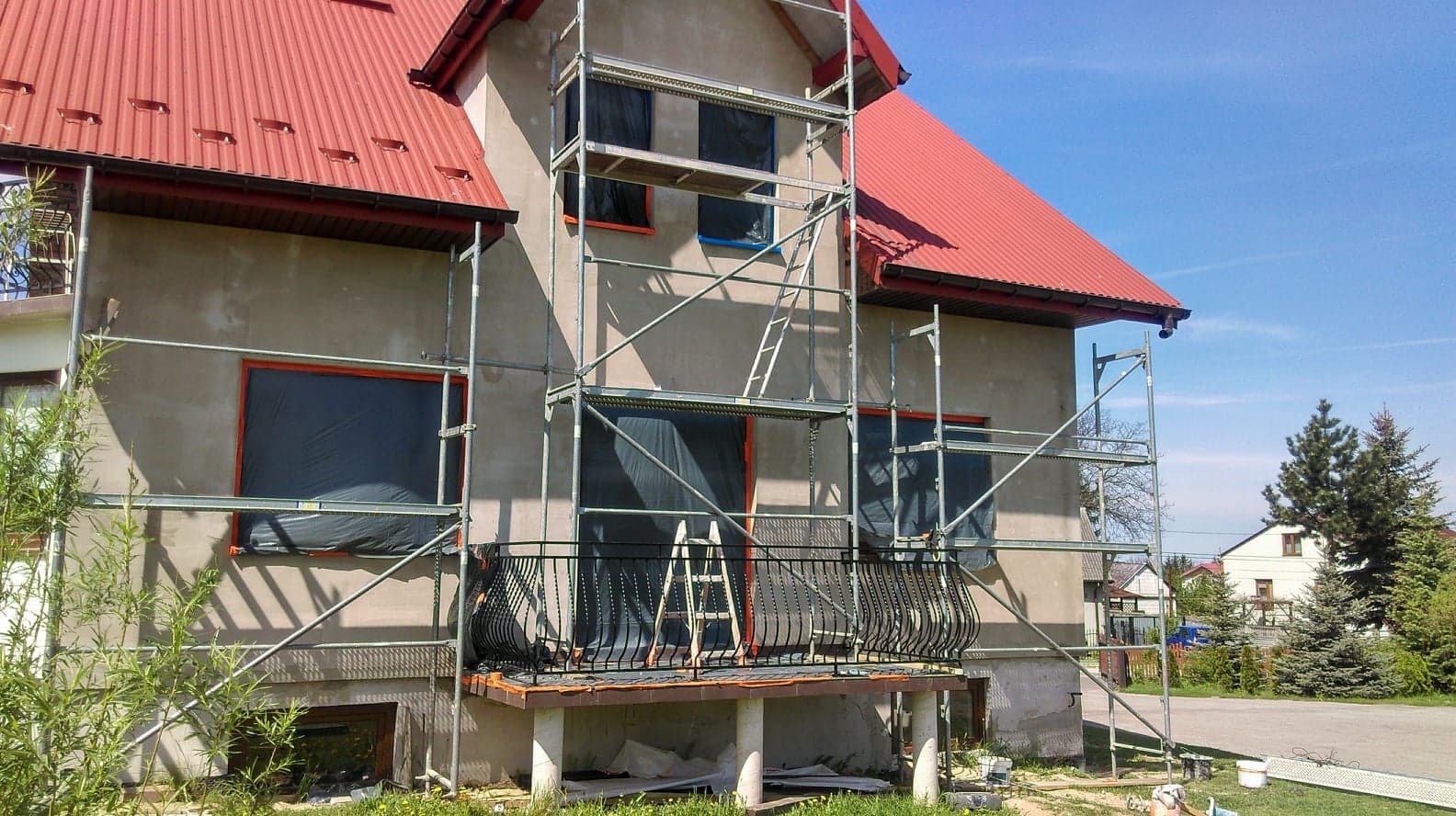 Dom jednorodzinny w trakcie przygotowania do malowania elewacji, okna zabezpieczone folią, rusztowania ustawione, widoczne niedoskonałości tynku.