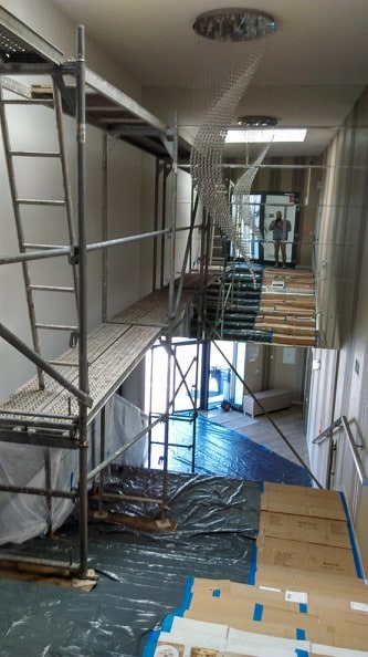 Korytarz biurowy w trakcie remontu, widoczne rusztowania, zabezpieczona podłoga folią, dekoracyjne elementy sufitowe w kształcie fal.