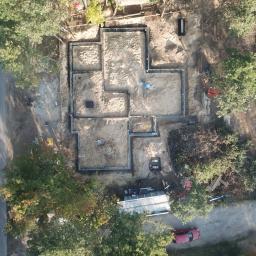 Rathcom - Widok z drona na plac budowy z wykopanymi fundamentami pod budynek, otoczony drzewami, z widocznym czerwonym samochodem na drodze dojazdowej.