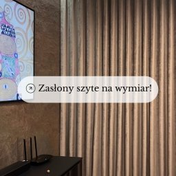 Dekoracja okien Gizela Mainka - Beżowe, plisowane zasłony na wymiar, wiszące od sufitu do podłogi, obok ściany z kamienia dekoracyjnego i czarnej szafki RTV.