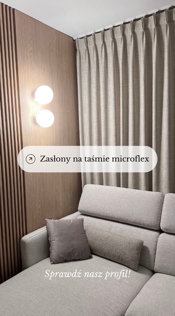 Beżowe, plisowane tekstylia okienne zawieszone na karniszu sufitowym, widoczne zza narożnika sofy w salonie z drewnianą ścianą akcentującą i okrągłymi lampami ściennymi.