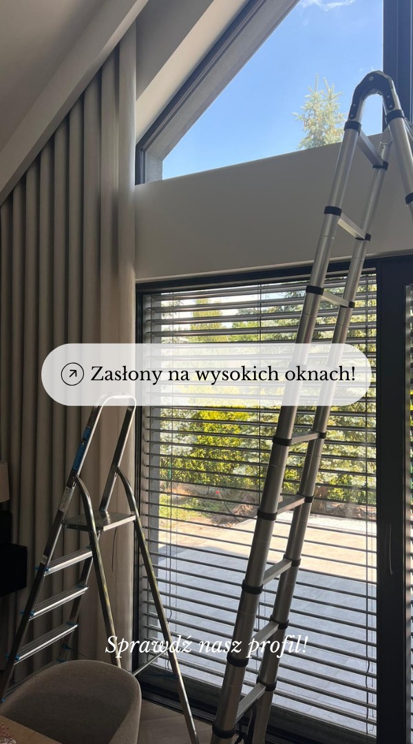 Wysokie okno z zamontowanymi beżowymi zasłonami i żaluzjami, widoczne drabiny monterskie.