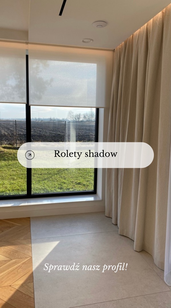 Jasne rolety w systemie dzień-noc i beżowe, drapowane zasłony w nowoczesnym wnętrzu z dużym oknem wychodzącym na zielony ogród.