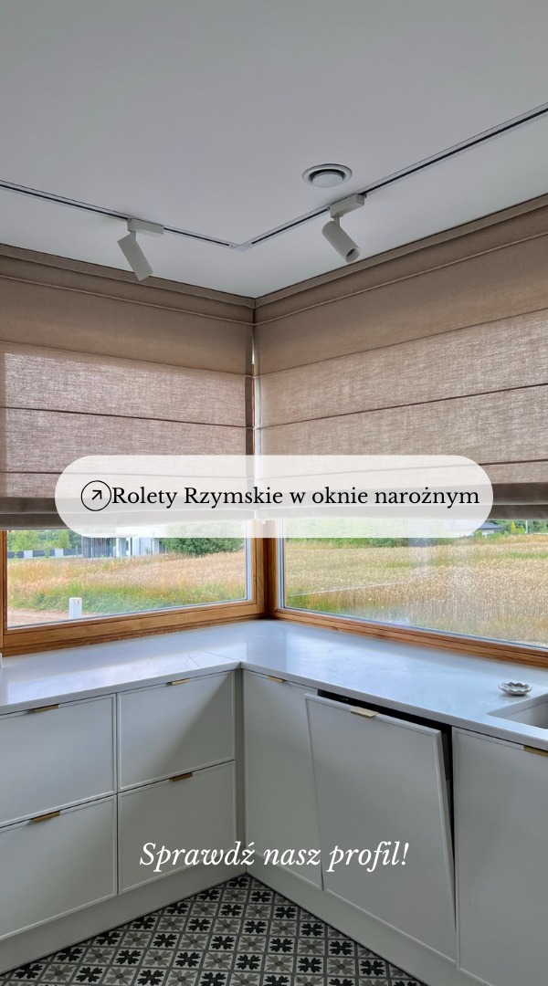 Beżowe rolety w oknie narożnym nad białymi szafkami kuchennymi z marmurowym blatem i wzorzystą podłogą, oświetlone reflektorami sufitowymi.