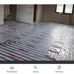 Rozłożona instalacja ogrzewania podłogowego z rur w nowym budynku w stanie surowym, widoczne rury grzewcze w regularnych odstępach na folii izolacyjnej i siatce zbrojeniowej.