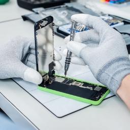 Naprawa Telefonów Tabletów Lublin - Naprawa iPhone'a 5c z zieloną obudową: technik w antystatycznych rękawicach dokręca śrubkę precyzyjnym śrubokrętem, ekran odseparowany od korpusu, widoczne wnętrze urządzenia.