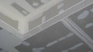 Szare płyty z widocznymi spoinami i śladami szpachlowania na suficie, ujęcie z dołu, w trakcie prac wykończeniowych.