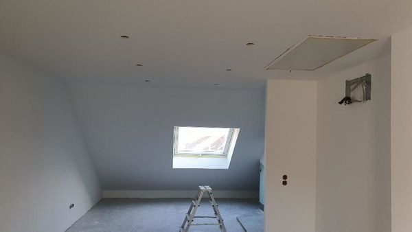 Poddasze po remoncie z oknem dachowym, widoczne punkty oświetleniowe w suficie, drabina i otwór rewizyjny w suficie.