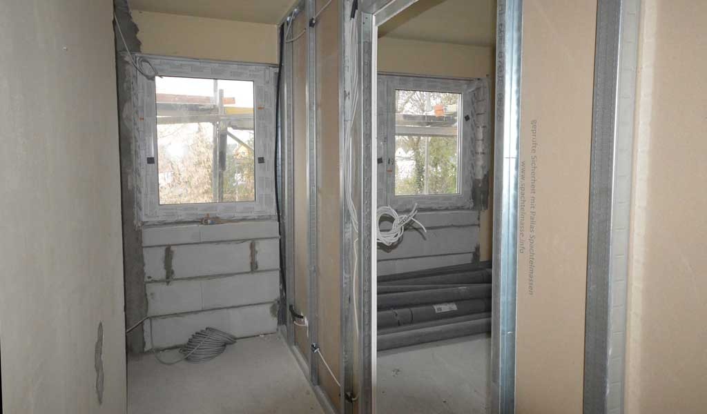 Wnętrze w trakcie remontu: widoczne profile metalowe konstrukcji ścianki działowej, okna z parapetami z bloczków betonowych, zwinięte kable elektryczne i rury wentylacyjne.