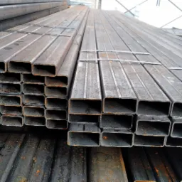 Stosy profili zamkniętych z surowej stali, spięte taśmami, widoczne ślady rdzy i niedoskonałości powierzchni.