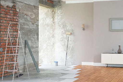 Remont pokoju: częściowo otynkowana ściana z cegłą, drabina, wałek do malowania, częściowo ułożony parkiet.