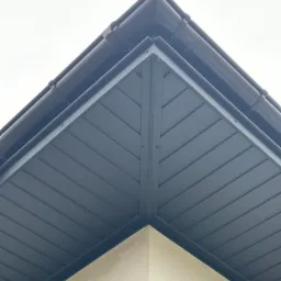 Szczegółowe ujęcie narożnika dachu z ciemną podbitką i rynną, widoczne mocowania elementów.
